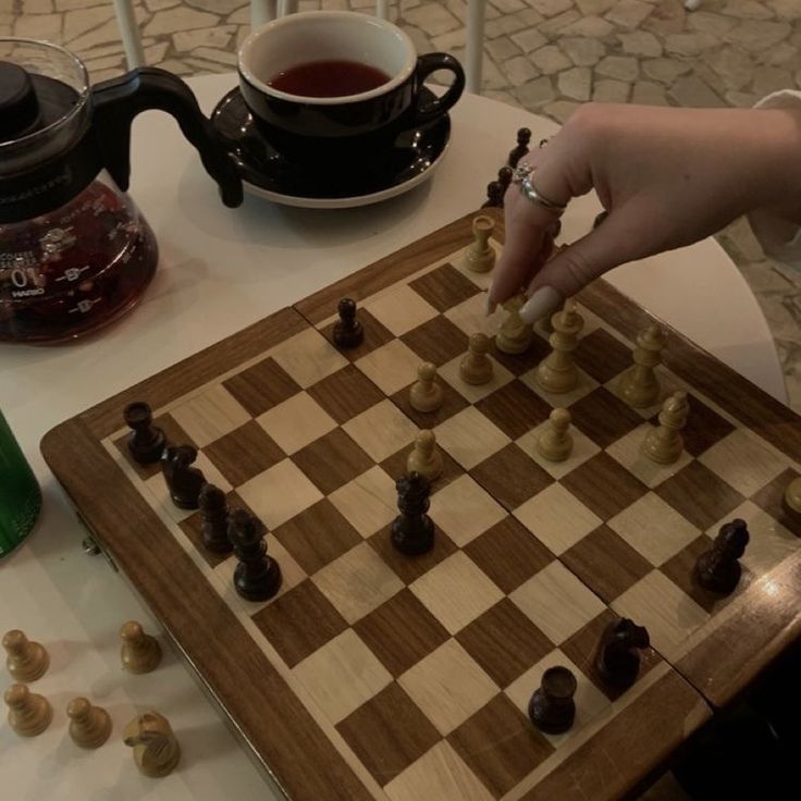 a person playing chess on a table with a cup of tea and kettles in the background