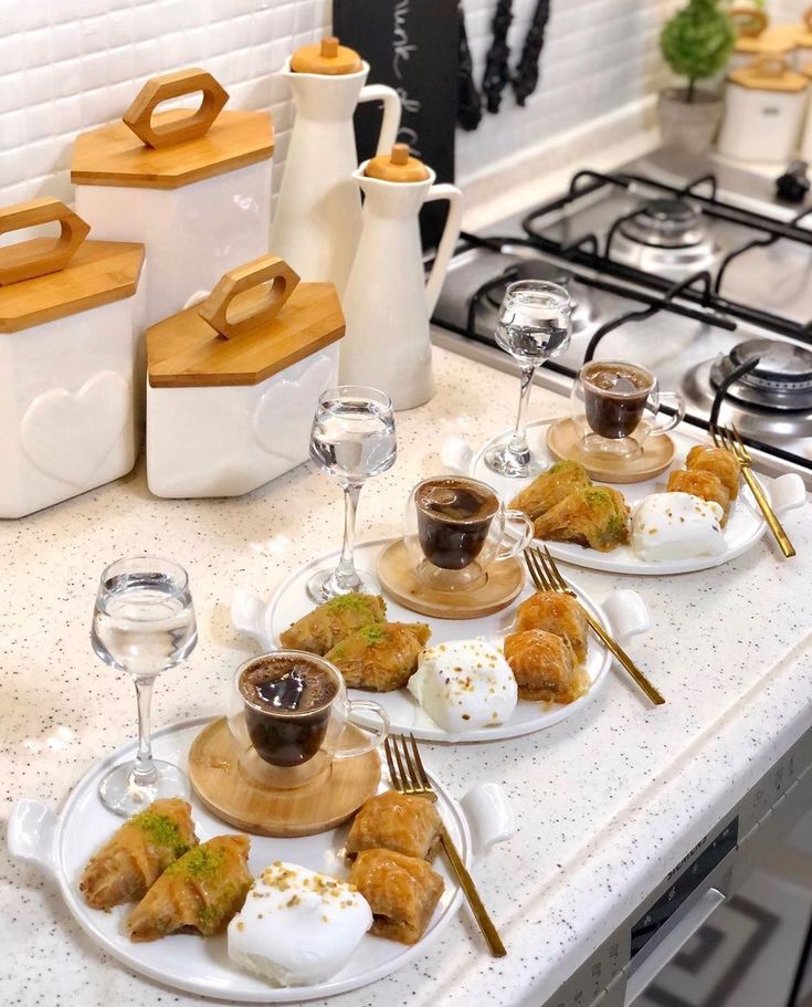 plates with food on them sitting on a kitchen counter top next to utensils and wine glasses