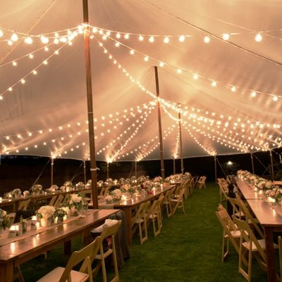 a large tent with tables and chairs set up for an outdoor dinner under string lights