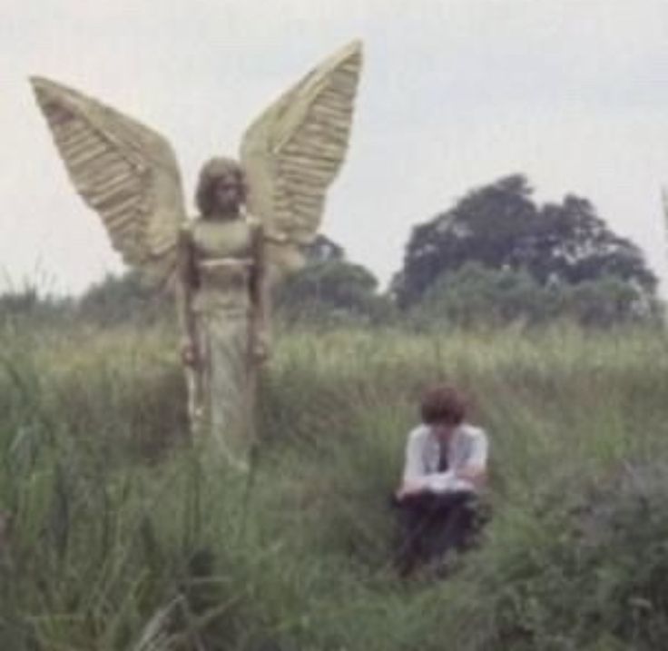 an angel statue sitting in the middle of a field next to a woman with wings