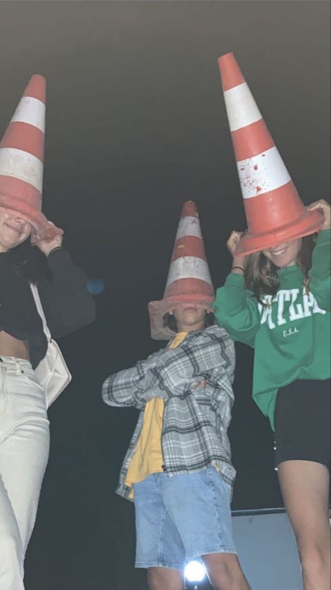 three children wearing orange and white traffic cones on their heads while standing next to each other