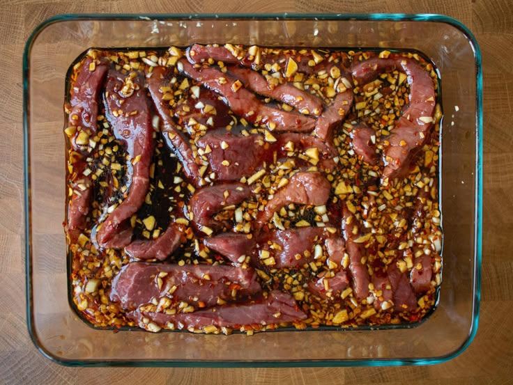 a glass baking dish filled with meat and nuts on top of a wooden table next to a knife