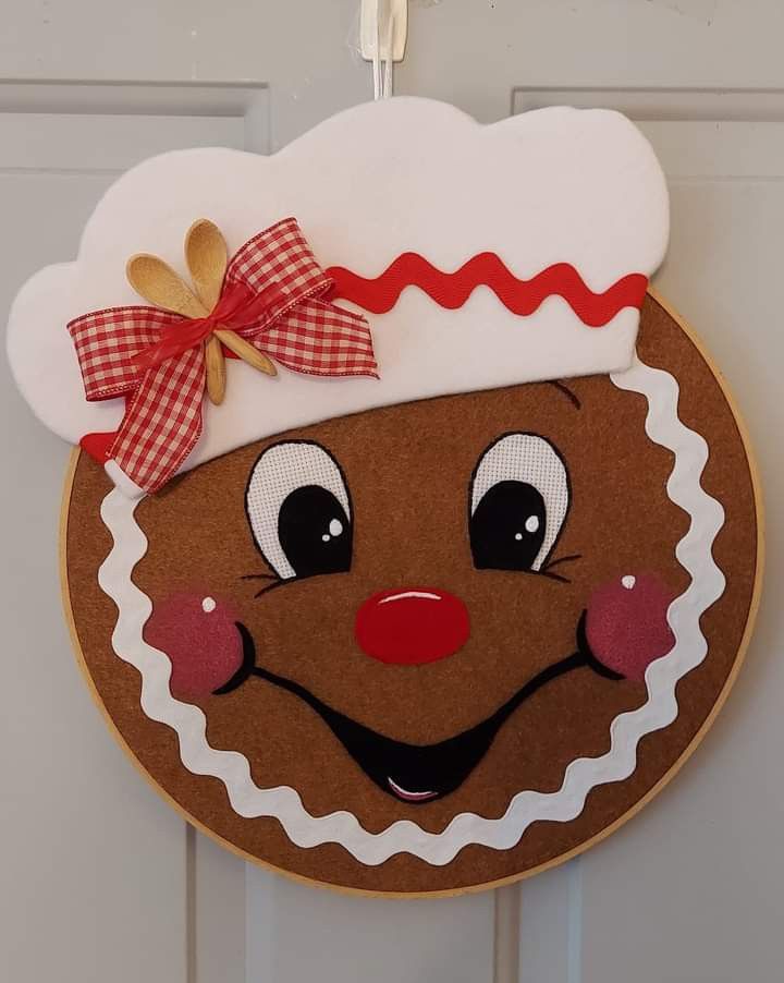 a door hanger with a gingerbread face on it's side and a red bow hanging from the front