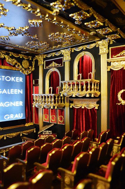 an auditorium with red velvet seats and gold decorations on the walls is shown in front of a large screen