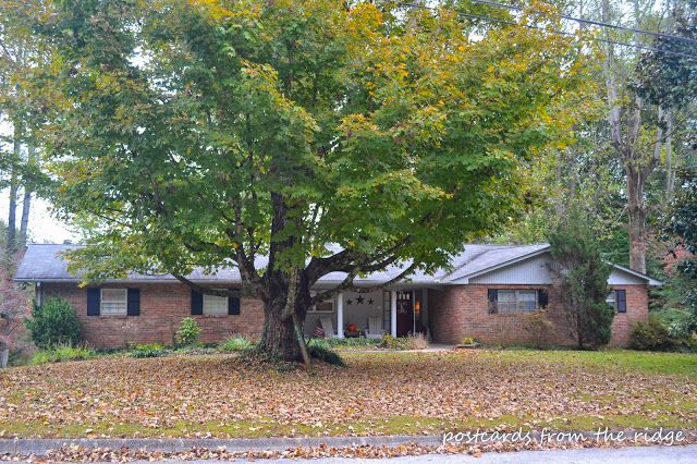 a house in the fall with leaves on the ground and trees around it's front yard