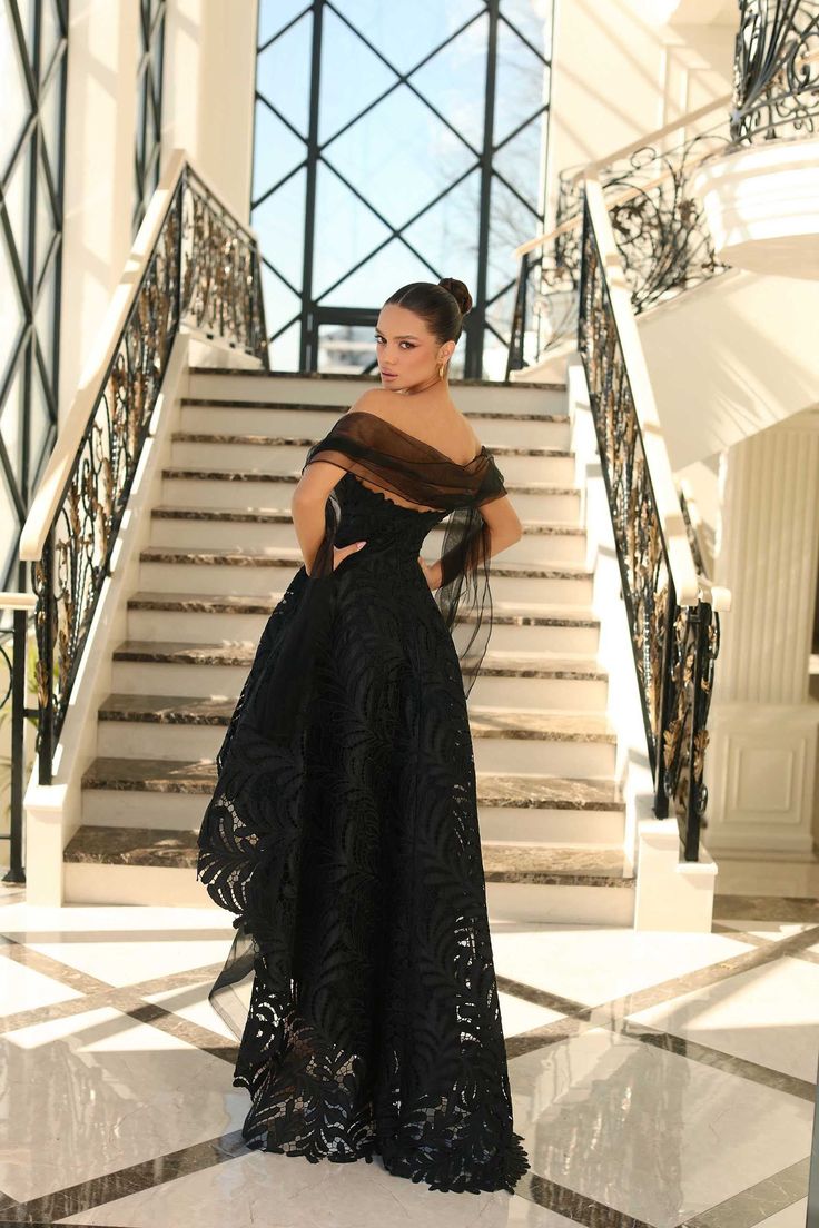 a woman standing in front of some stairs wearing a black dress with an off the shoulder neckline