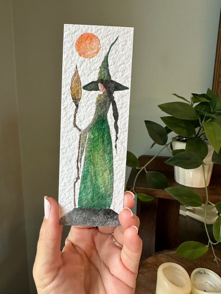 a person holding up a card with a painting on it