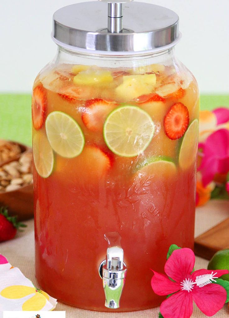 a pitcher filled with fruit and lemonade on top of a table next to flowers