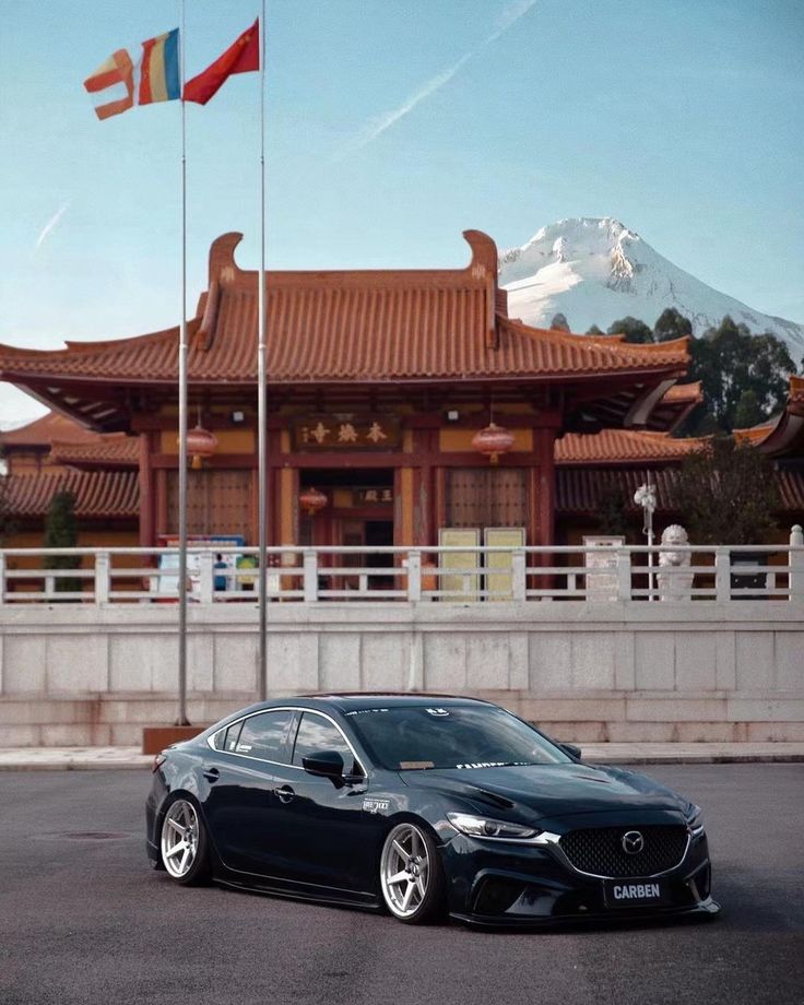 a car parked in front of a building with two flags on it's poles