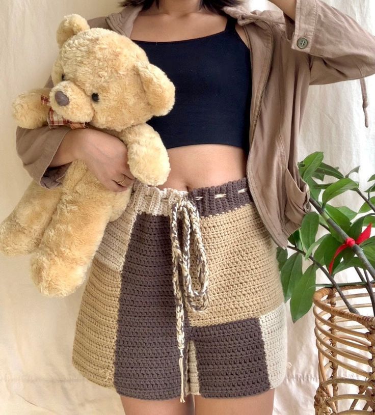 a woman holding a teddy bear in her right hand and wearing a skirt on the other side