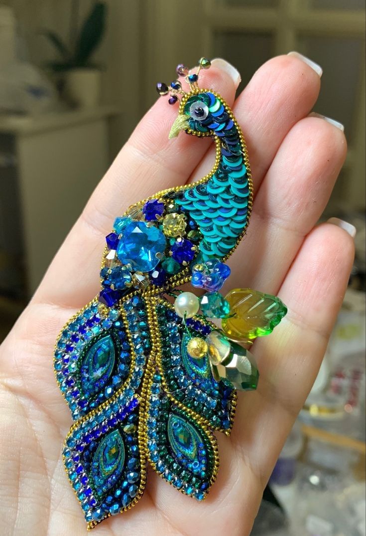 a peacock brooch sitting on top of a person's hand