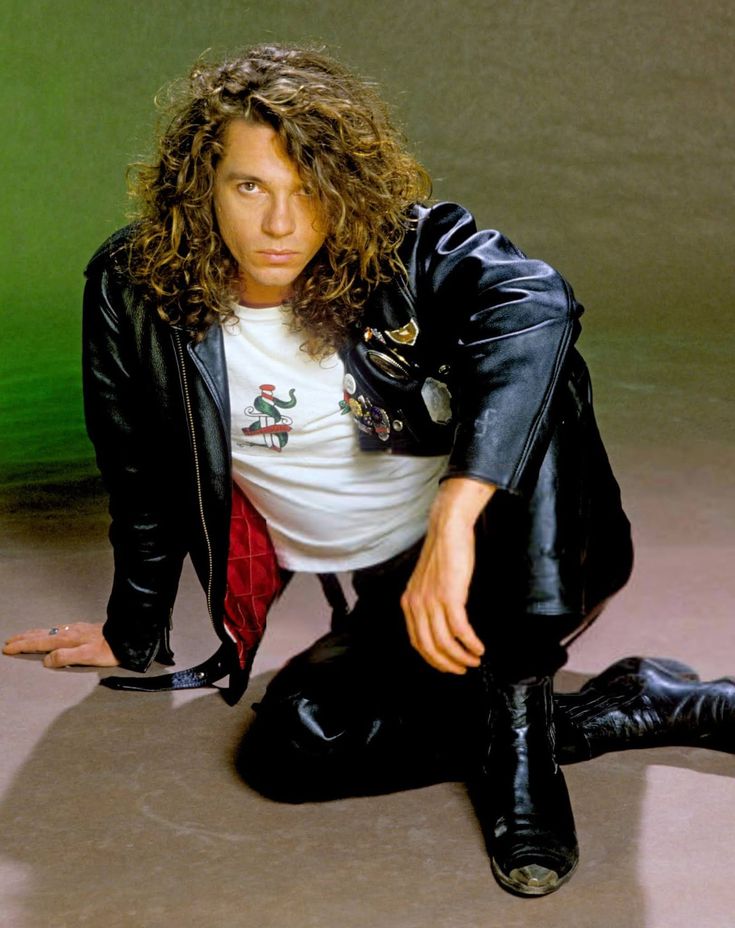 a man sitting on the ground with his legs crossed and wearing black leather pants, white t - shirt and jacket