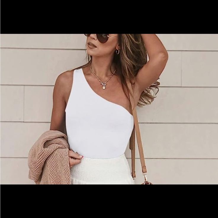 a woman wearing a white dress and carrying a brown purse standing in front of a brick wall