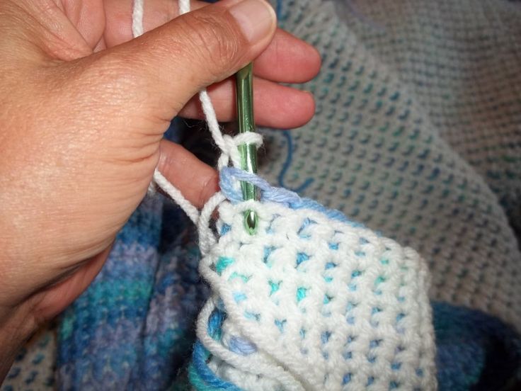 someone is crocheting the end of a blue and white knitted object with yarn