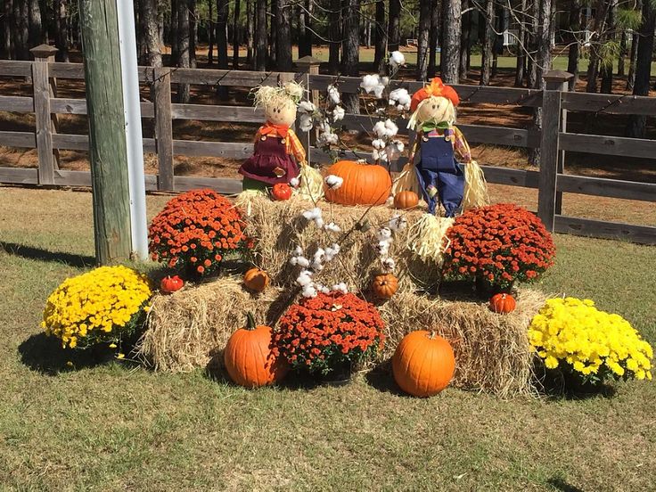 two scarecrows sitting on hay bales with pumpkins and flowers