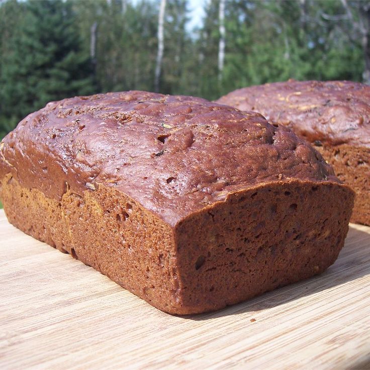 two loafs of bread sitting on top of a wooden cutting board next to trees