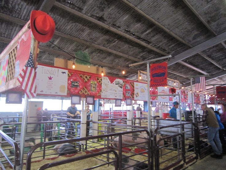 several people are standing around in an indoor area with signs on the walls and cattle pens