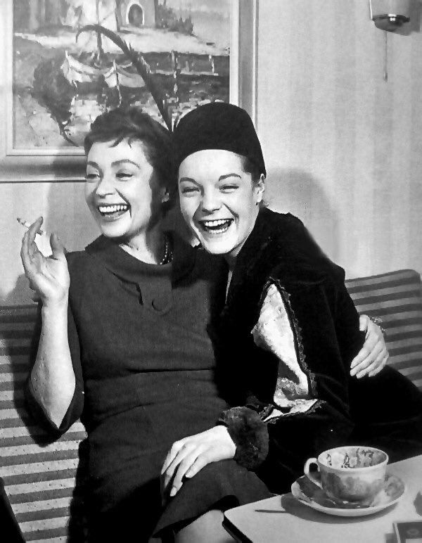 two women sitting next to each other on a couch with coffee cups in front of them