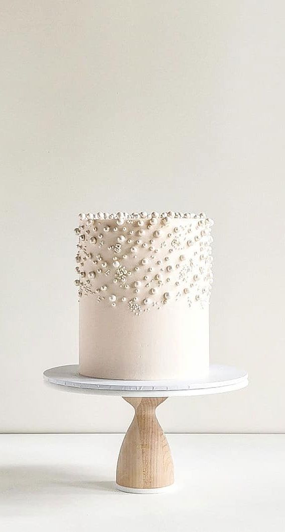 a white cake with pearls on top sitting on a wooden stand in front of a wall