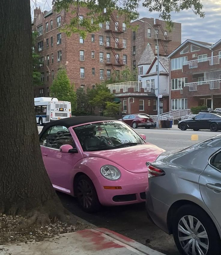 a pink car parked next to a tree on the side of a road near some buildings