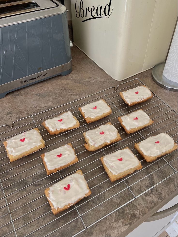 six square cookies with white frosting on a cooling rack next to a toaster