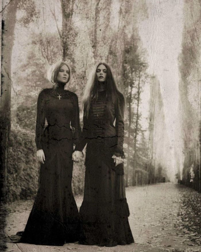 two women in long dresses standing next to each other on a path through the woods