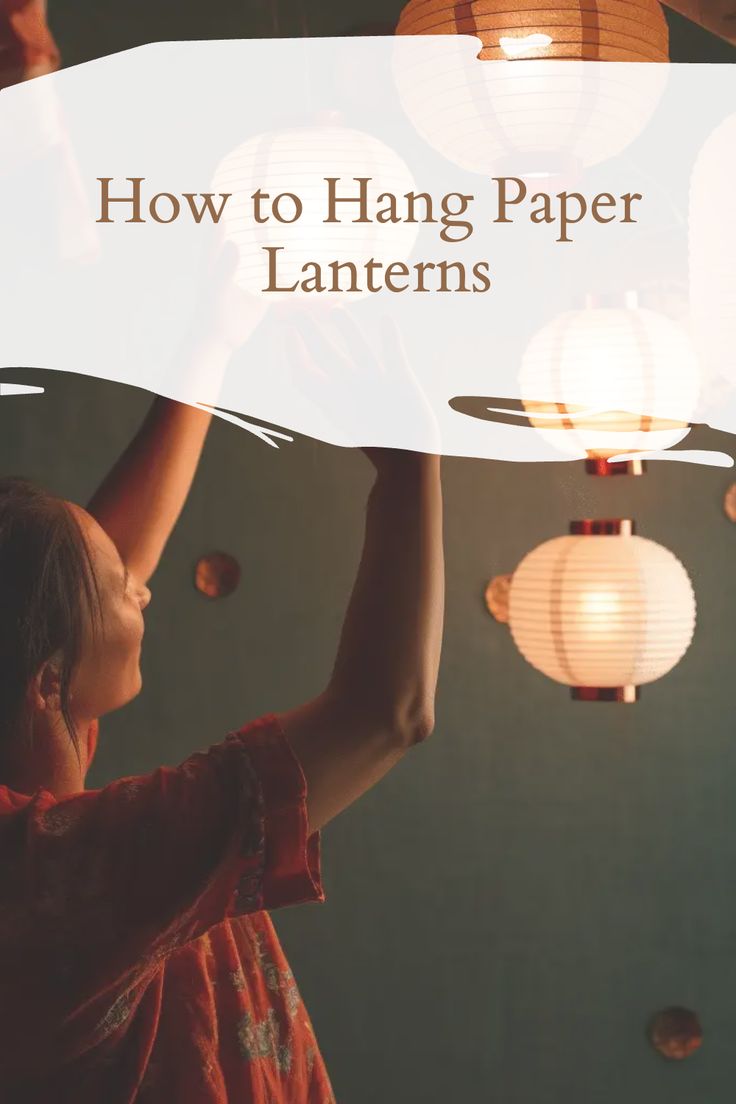 a girl reaching up to the ceiling with paper lanterns in front of her and text overlay reading how to hang paper lanterns