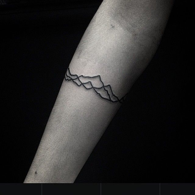 a black and white photo of a mountain tattoo on the left inner arm, with mountains in the background