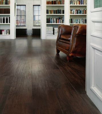 an empty room with bookshelves, leather chair and wooden flooring in it