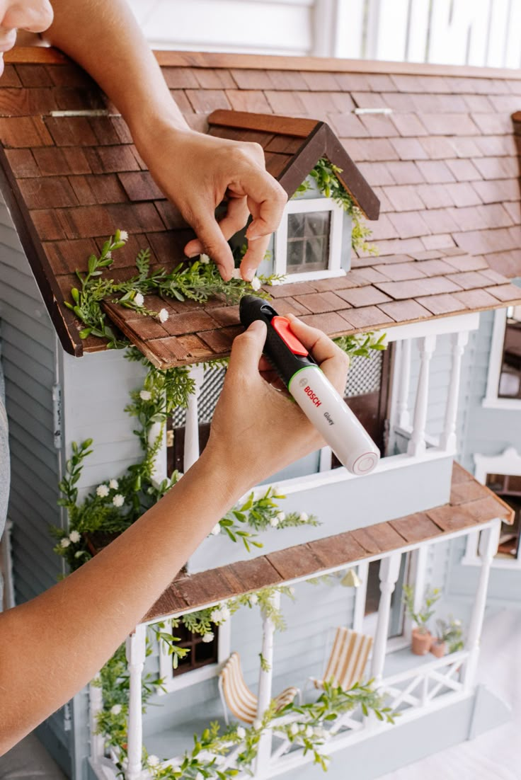 someone is painting the outside of a dollhouse with greenery on it's roof