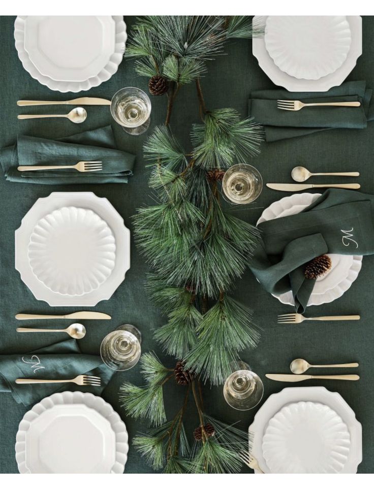 the table is set with white plates and green napkins, silverware, pine cones, and evergreen branches