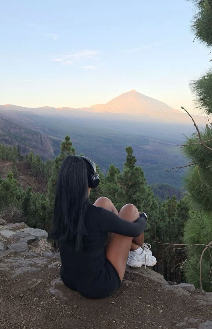 a woman sitting on top of a rock next to a forest