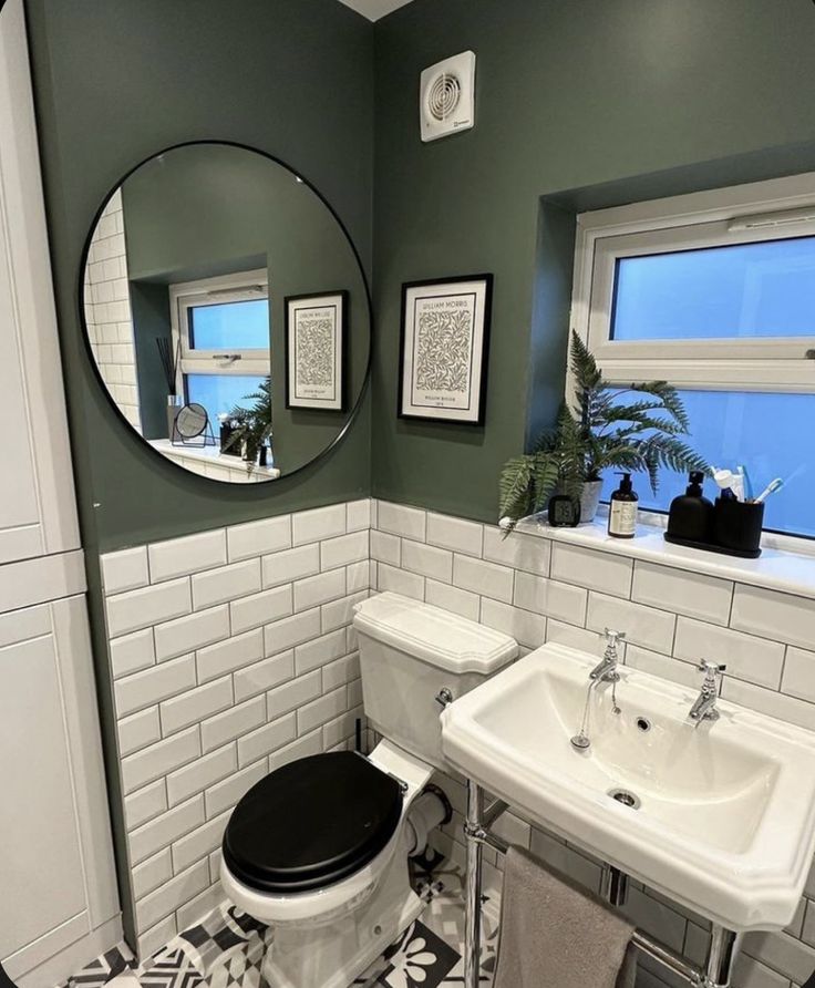 a white toilet sitting next to a sink in a bathroom under a large round mirror