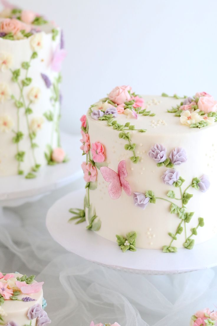 there is a white cake with pink and purple flowers on the frosting, along with other cakes