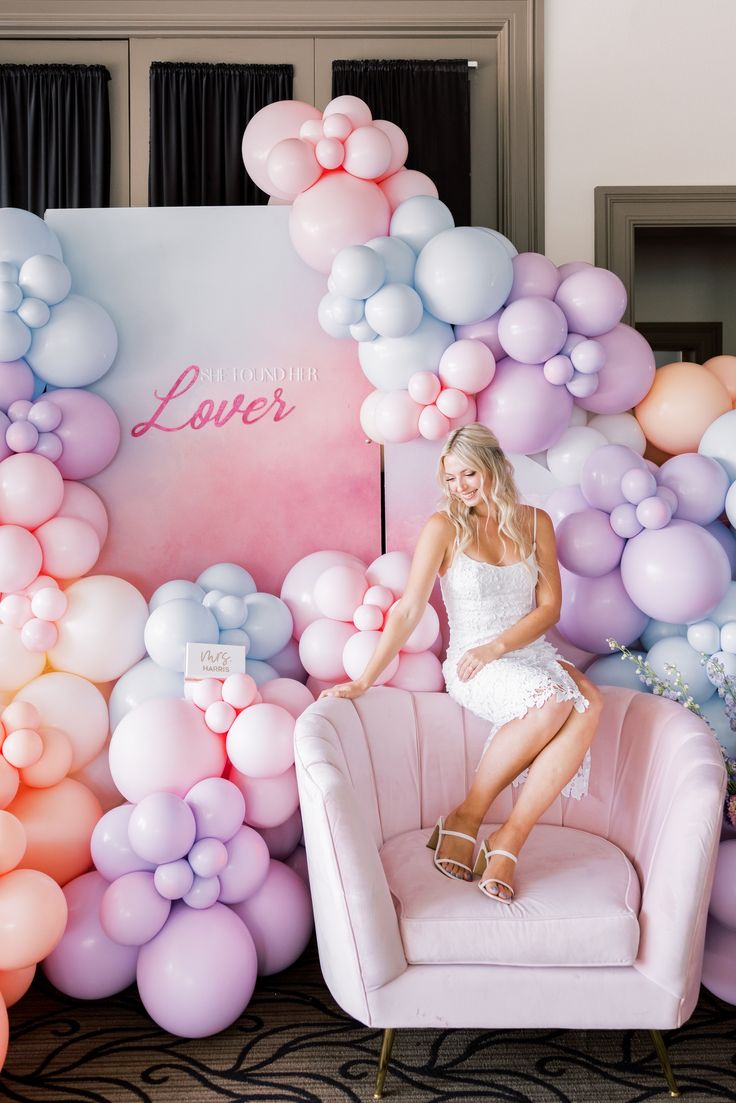 a woman sitting on a pink chair in front of balloons