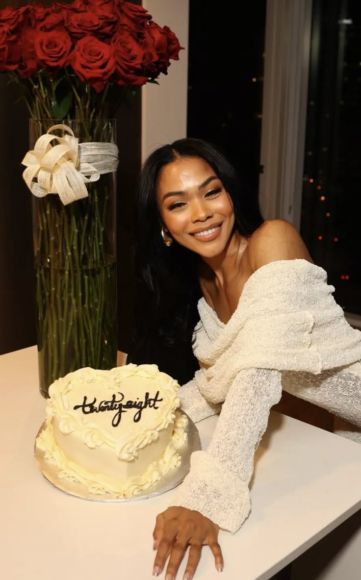 a woman leaning on a counter next to a cake and vase with roses in it