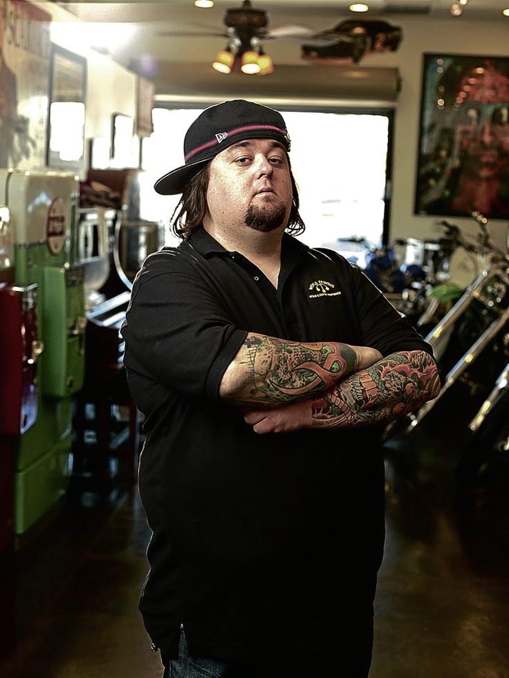 a man with tattoos standing in a room full of motorbikes and other motorcycles