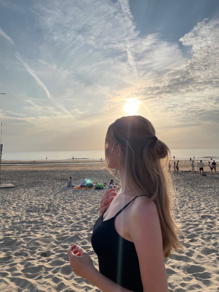 a woman standing on top of a sandy beach next to the ocean with people in the background