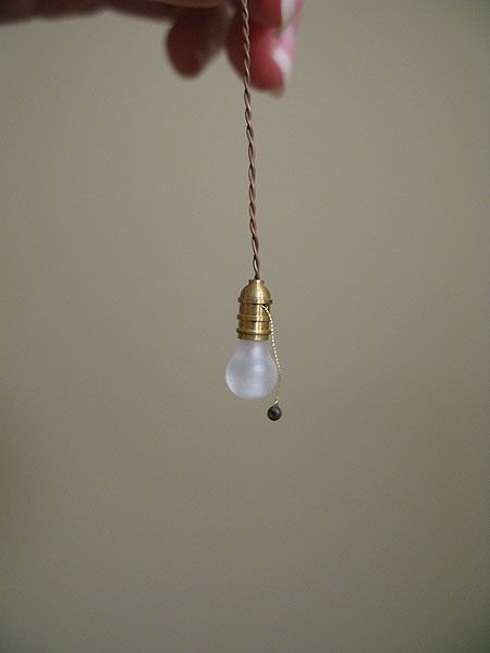 a hand holding a light bulb with a string attached to it and an object hanging from the ceiling