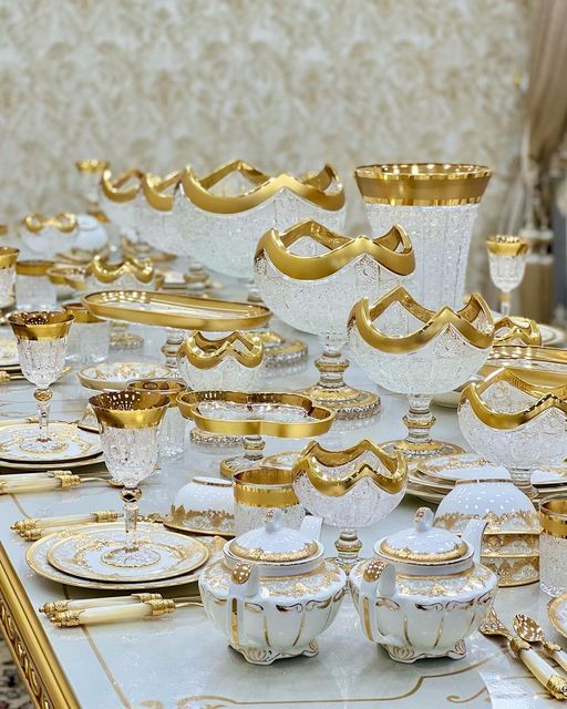 a table topped with lots of white and gold dishes covered in golden trimmings