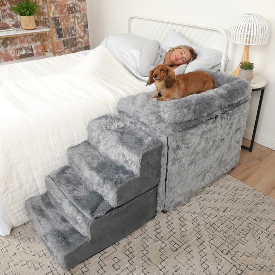 a woman laying in bed with her dog on top of the pet bed that's made to look like stairs