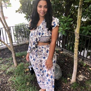 a woman standing in front of a tree wearing sandals and a blue floral print dress