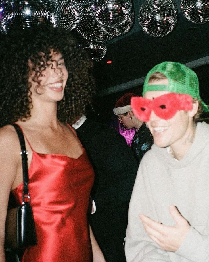 two women in red and green masks standing next to each other with disco balls hanging from the ceiling behind them