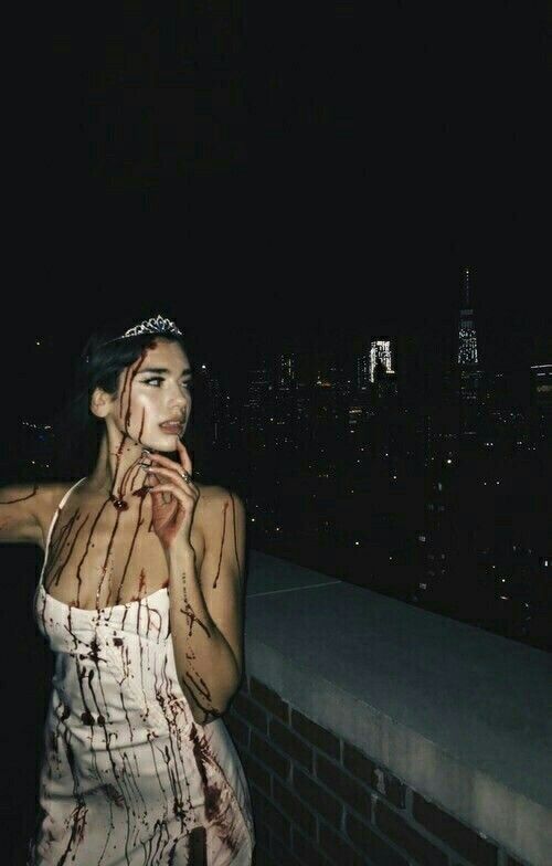 a woman with blood all over her body standing on top of a roof at night