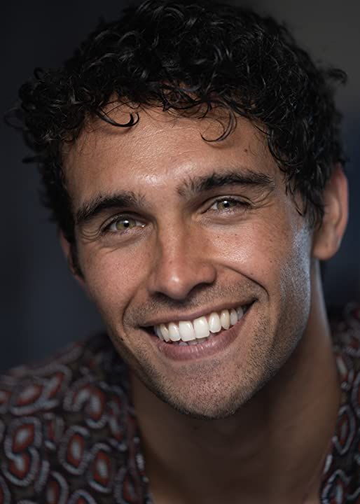 a man with curly hair smiling at the camera while wearing a patterned shirt and tie