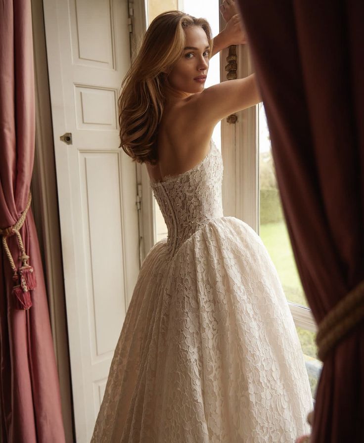 a woman in a wedding dress looking out the window