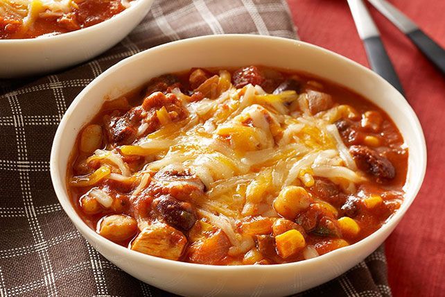 a white bowl filled with chili and cheese on top of a checkered table cloth