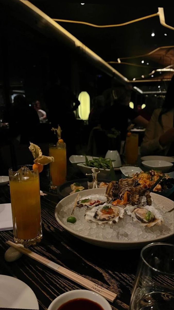 a plate with oysters on it sitting on a table next to drinks and glasses