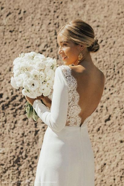 a woman in a white wedding dress holding a bouquet of flowers and looking off into the distance