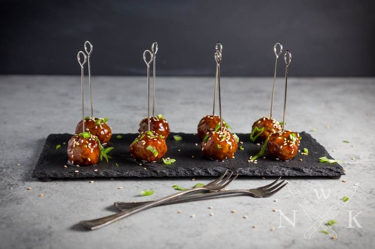 small appetizers are arranged on a black plate with silver forks and garnishes